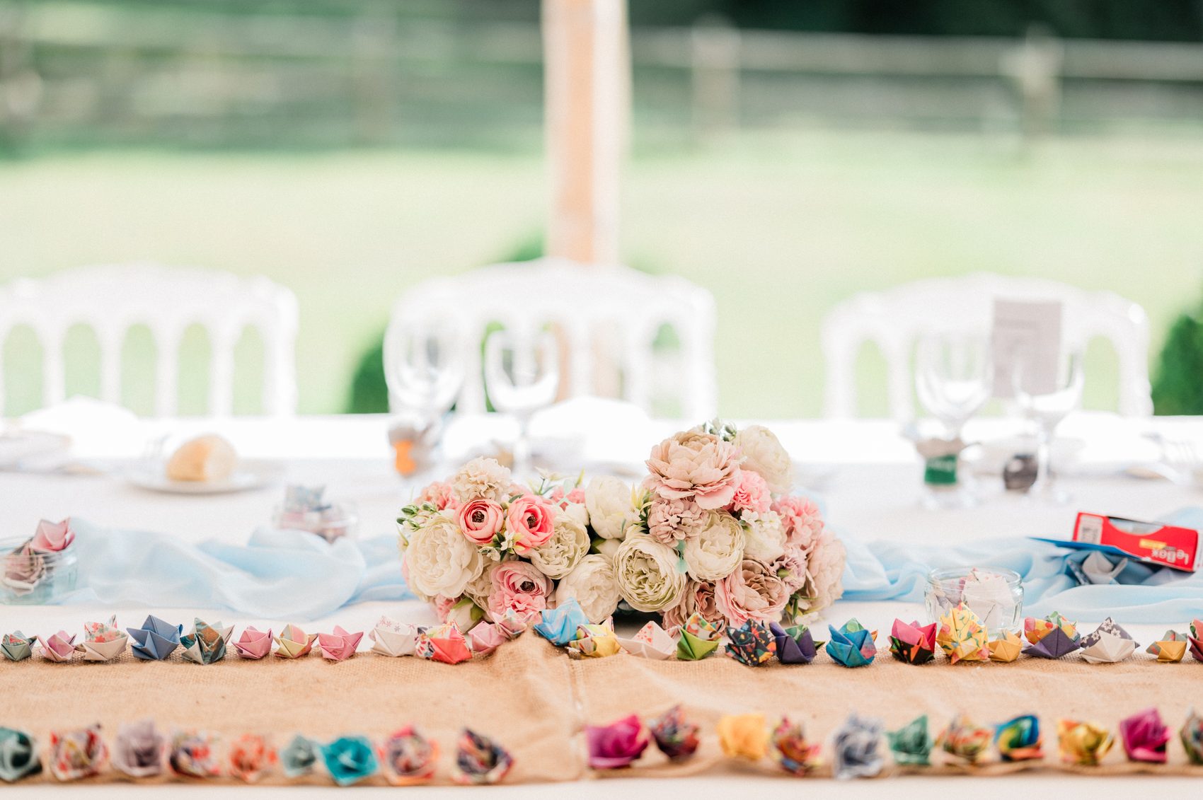 Table de mariage colorée sous le chapiteau du Château de Séréville, fleurs et origamis, verdure en fond