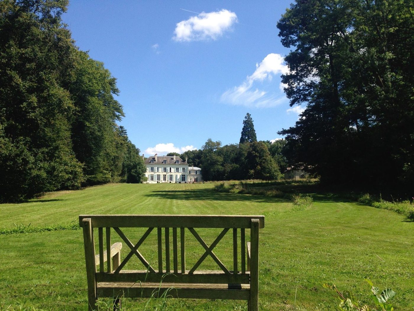 Un banc de bois dans l'allée du parc, la façade du château au fond