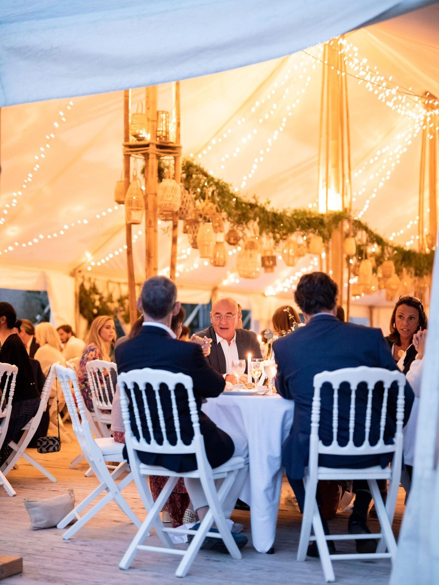 Dîner de mariage sous le chapiteau bambou illuminé de guirlandes à la nuit tombée