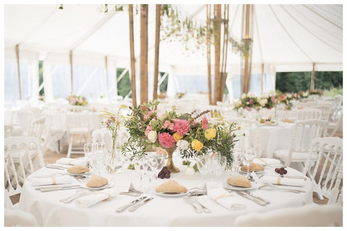 Tables de mariage dressées sous les mâts de bambou, fleurs et lumière naturelle